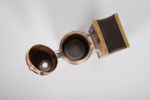 Enfumoir en cuivre ouvert vu du dessus, laissant apparaître la cuve et la grille de fond avant le chargement du combustible
